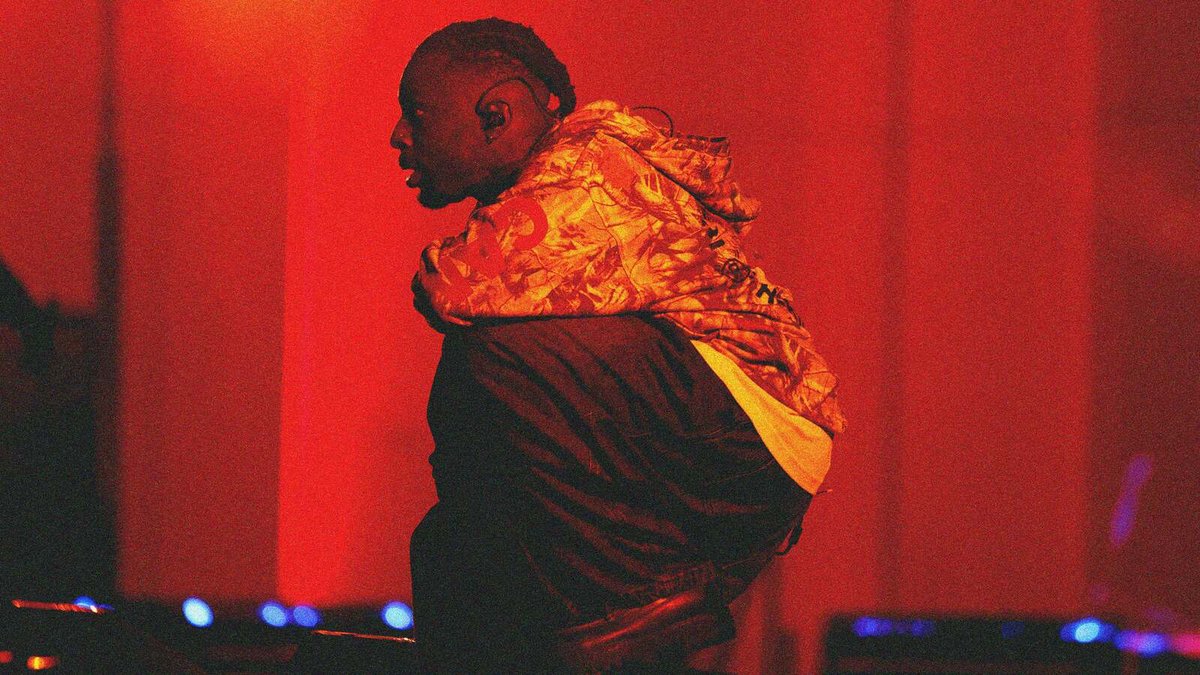Isaiah Rashad in a camo hoodie performing onstage under deep red stage lights
