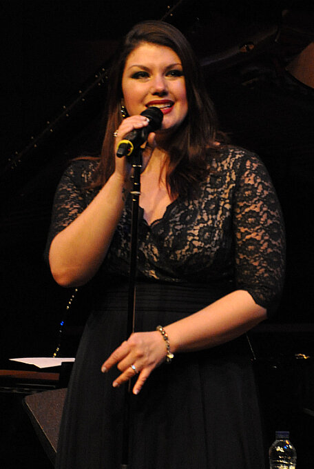 Singer in a black lace dress holding a microphone on a dimly lit stage