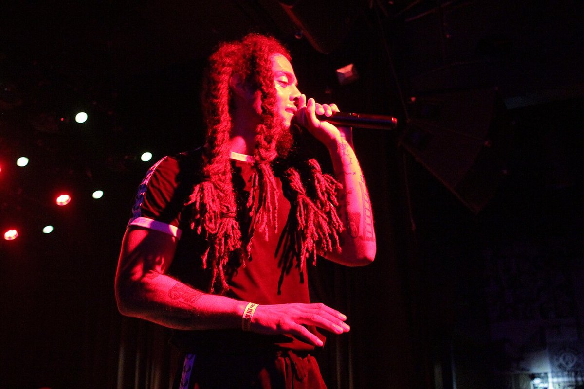 A singer with long hair performing into a microphone under red light
