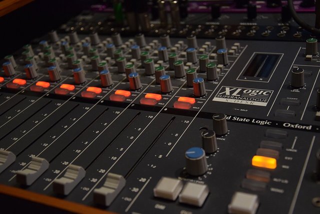 Close-up of an analog mixing desk with rows of knobs, faders and a lit orange button