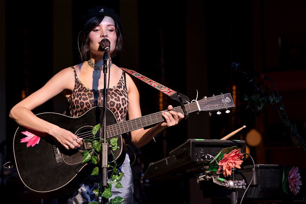 A singer with an acoustic guitar at a microphone on a dark stage