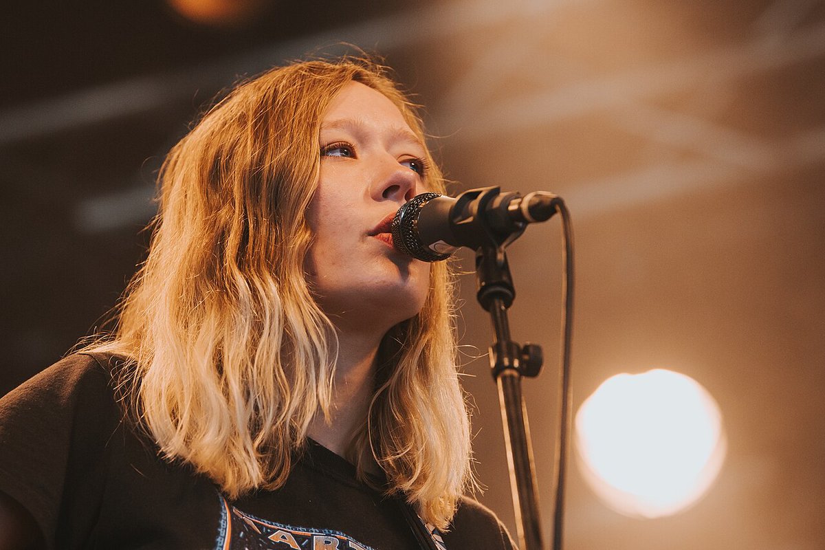 Julia Jacklin singing into a microphone on stage under warm light