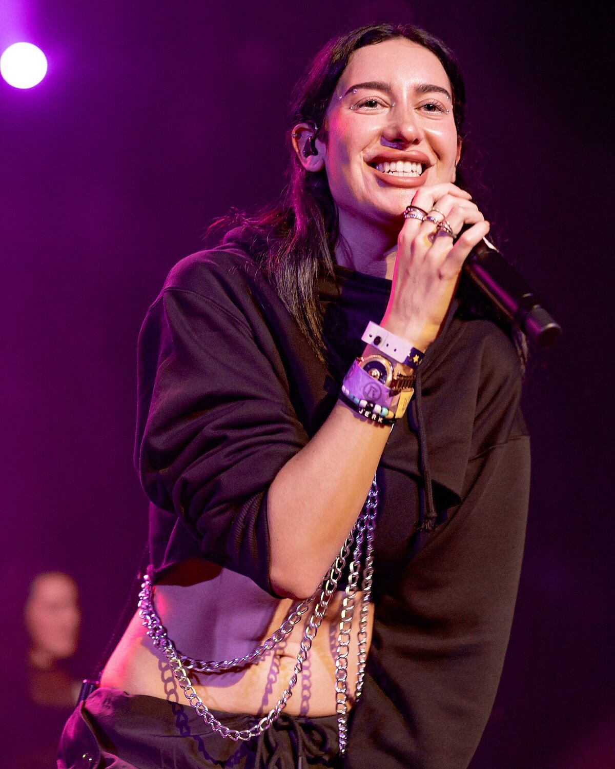 Julia Wolf smiling and singing into a handheld microphone on a purple-lit stage