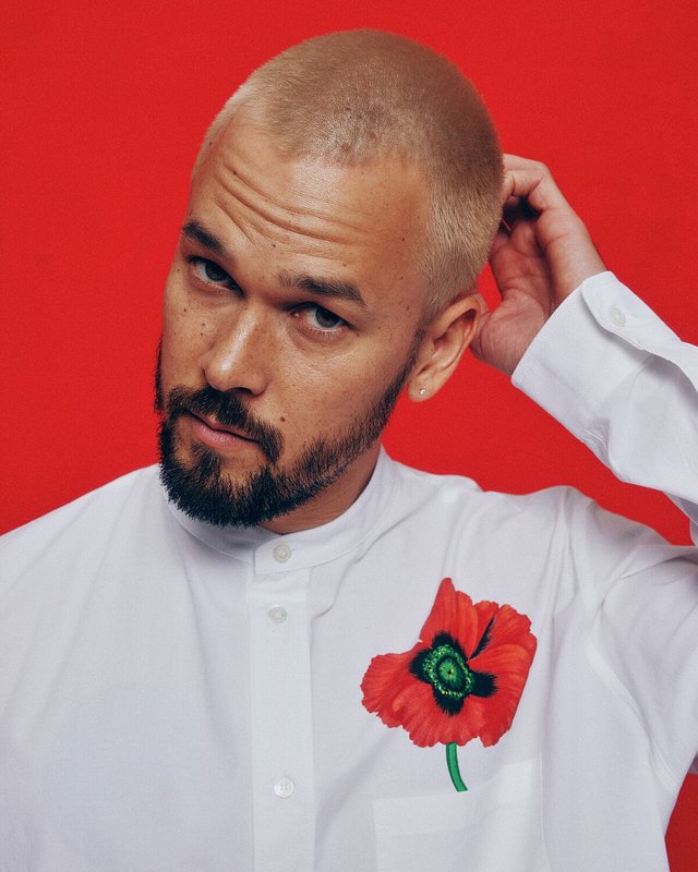 Portrait of Justin Nozuka in a white shirt with a red poppy print against a red backdrop