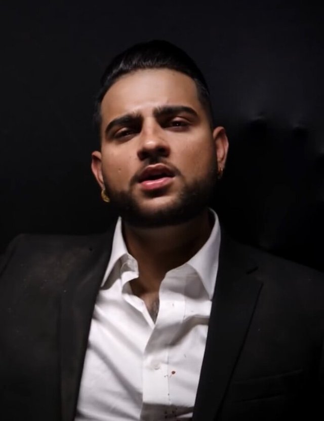 Portrait of Karan Aujla in a dark jacket and white open-collar shirt against a black backdrop