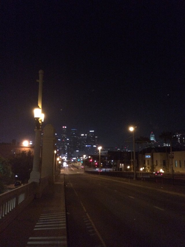 Night view down a lamp-lit street toward the lit downtown Los Angeles skyline