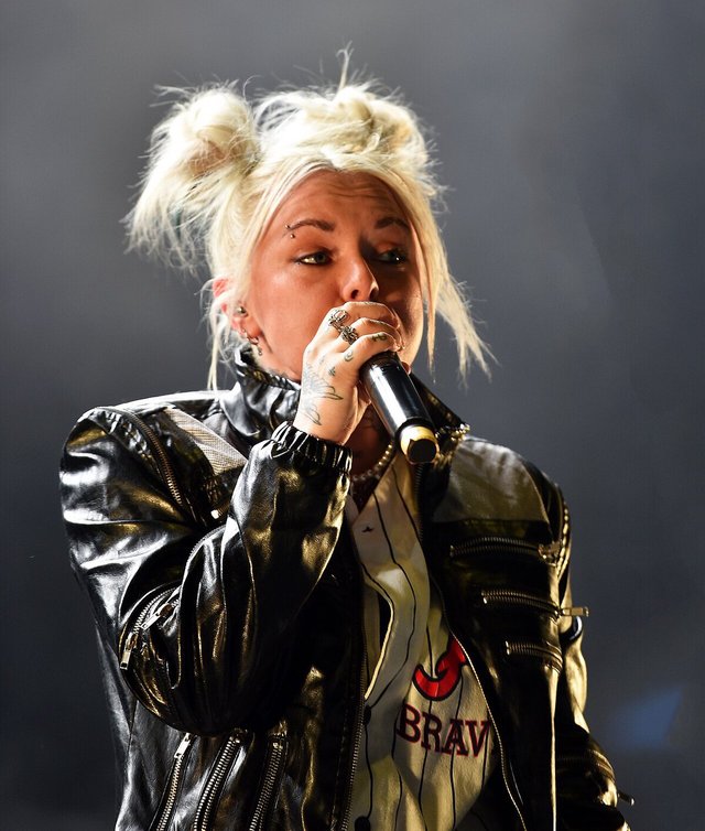 Lauren Sanderson singing into a microphone on stage, wearing a black leather jacket with her blonde hair in two buns