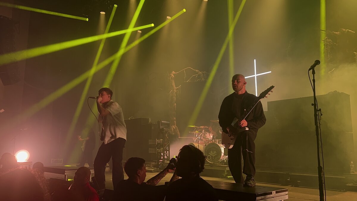 Knocked Loose on stage, a vocalist at the mic and a guitarist under green stage beams