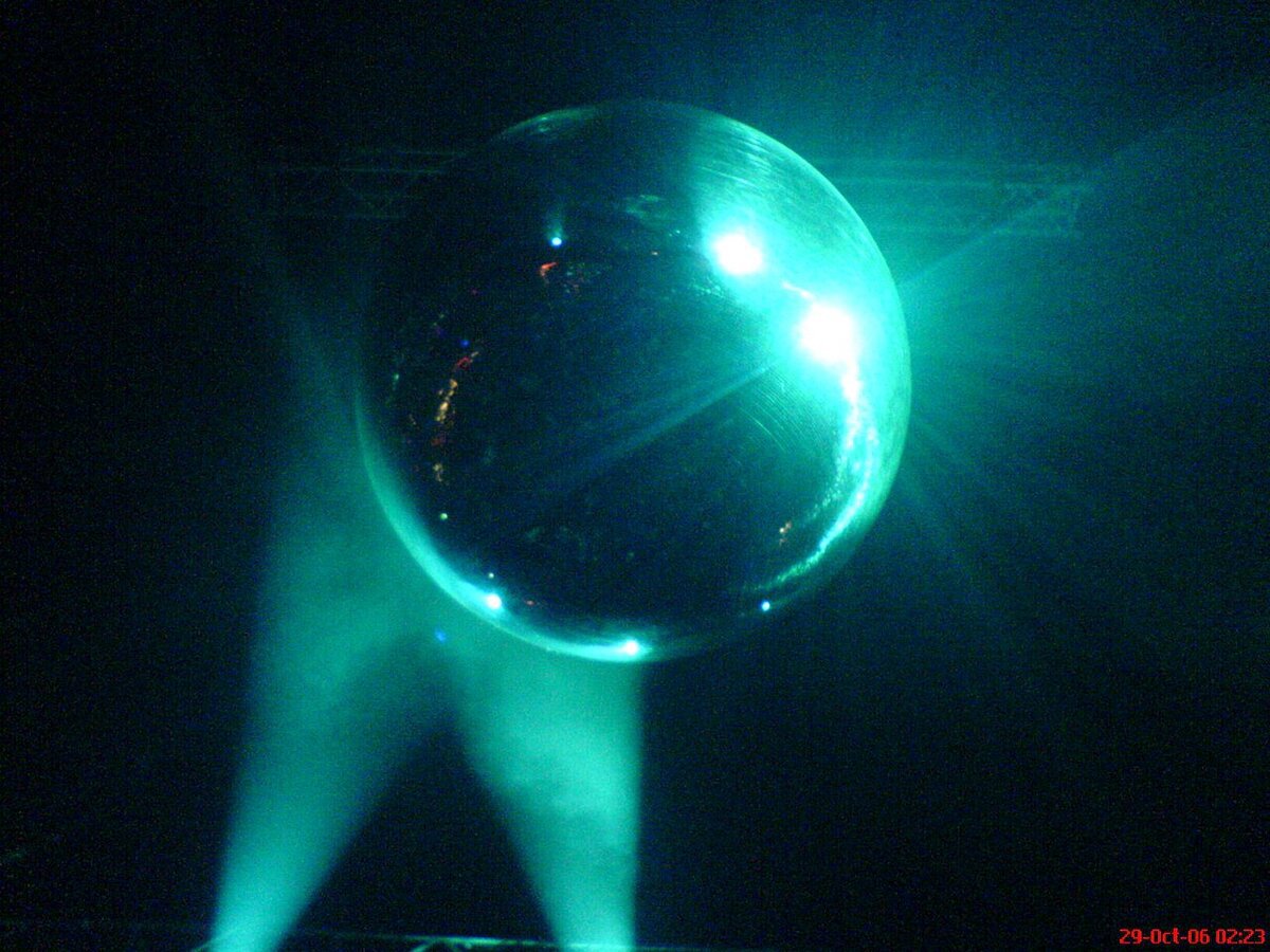 A mirrored disco ball lit in green stage light against a dark room