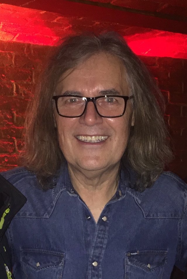 Portrait of Leonid Vorobyev, the band's founder, smiling in glasses and a denim shirt against a red brick wall