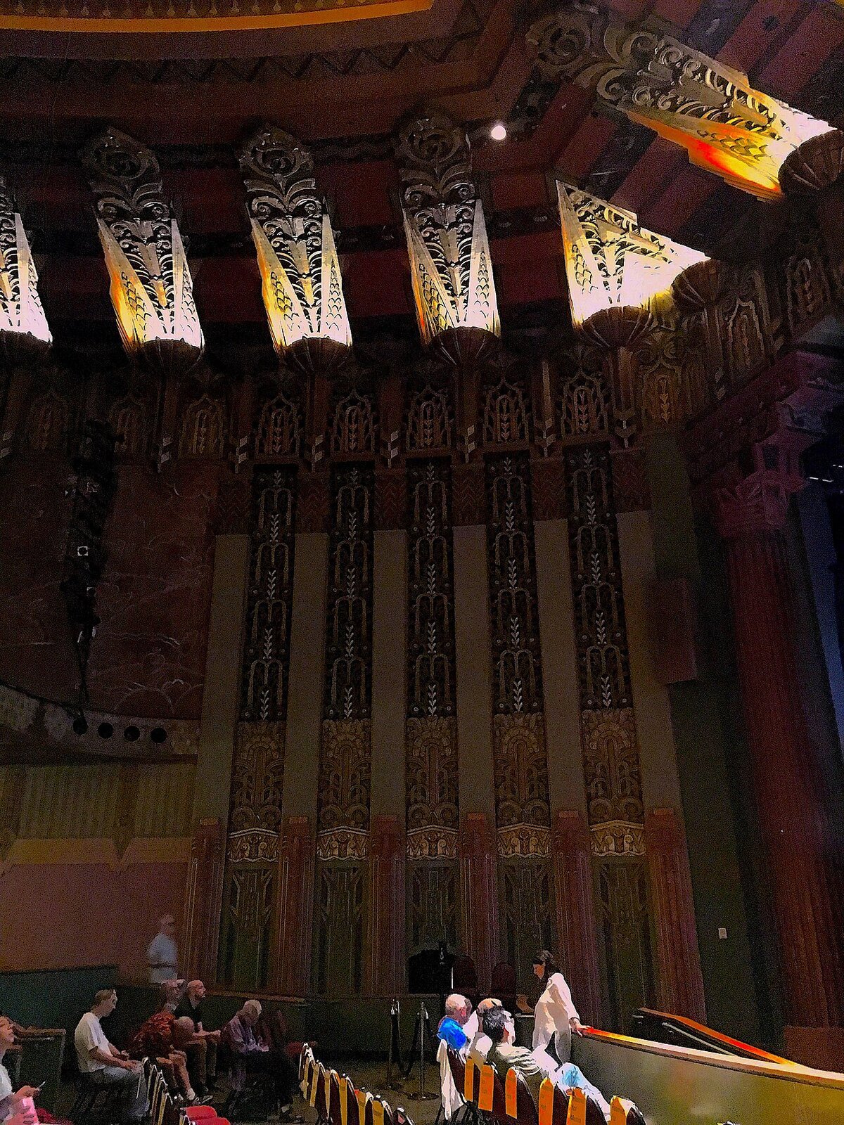 Art deco interior of The Wiltern with ornate gilded columns and lit ceiling fixtures above the seating area