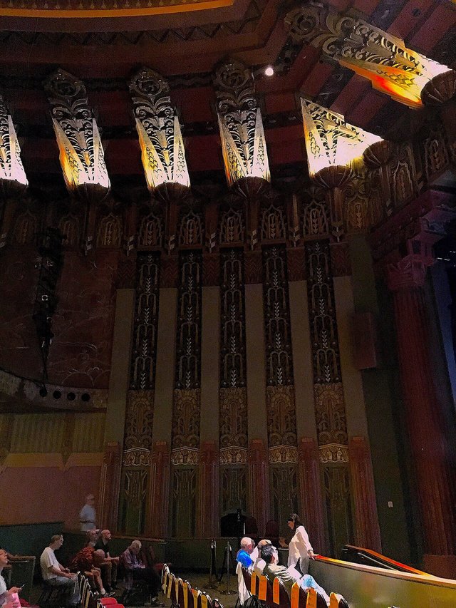 Art deco interior of The Wiltern with ornate gilded columns and lit ceiling fixtures above the seating area