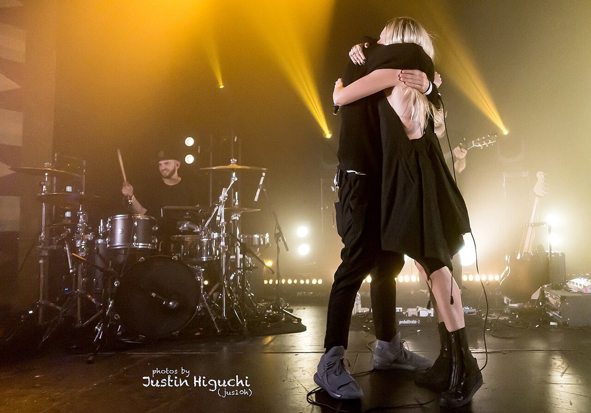 A drum kit on a stage lit amber, with two performers embracing in front of it