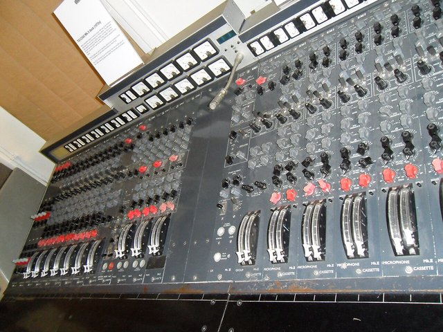 A large vintage analog mixing console with rows of faders and knobs in a recording studio control room