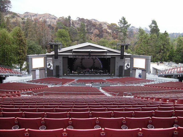 Rows of red seats facing the stage of the Greek Theatre with wooded hills behind it