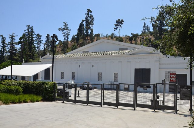 Whitewashed exterior of the Greek Theatre in Griffith Park with a hillside of trees behind it