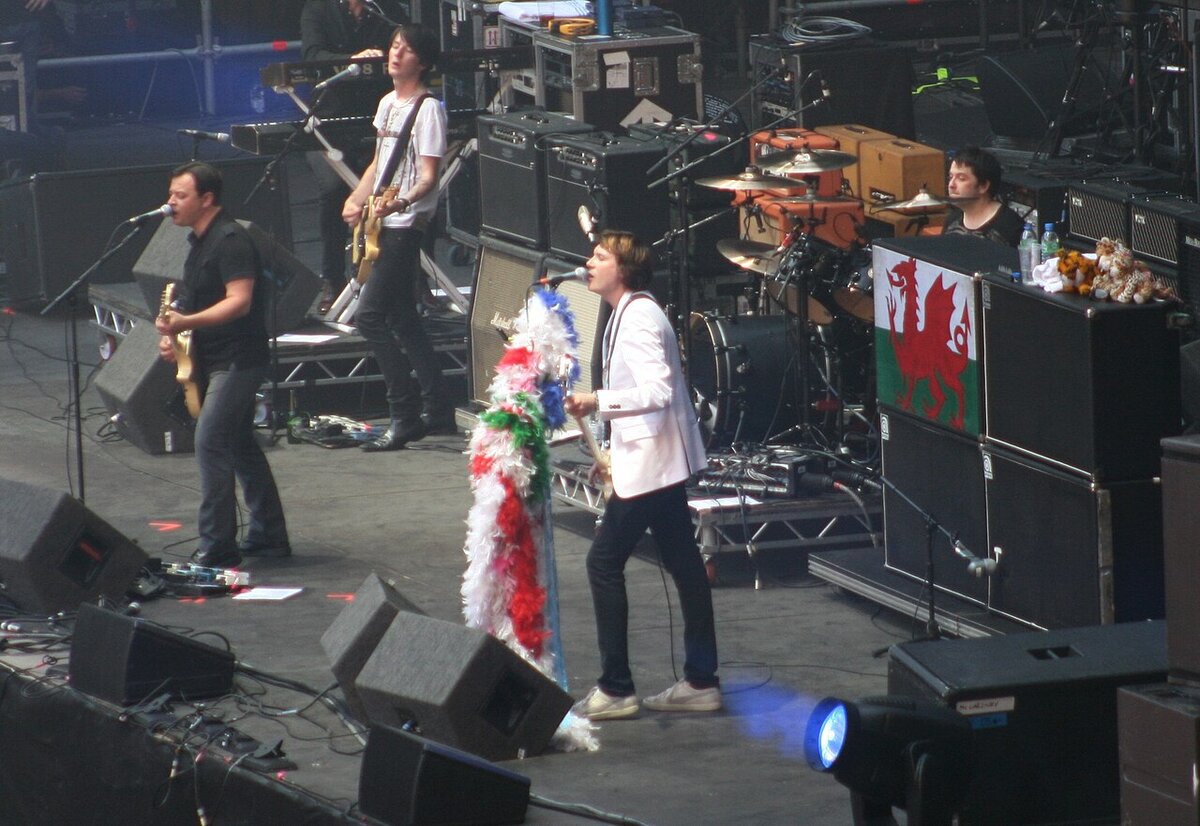 Manic Street Preachers performing on a large stage with guitarists, a singer in a white jacket and a drummer behind