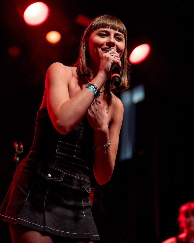 Singer in a black dress holding a microphone on a stage lit in red
