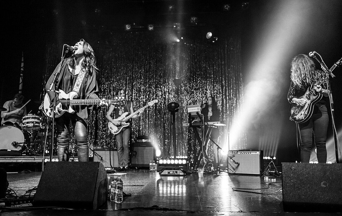Michelle Branch singing and playing electric guitar on stage with her band under white spotlights, black and white photo