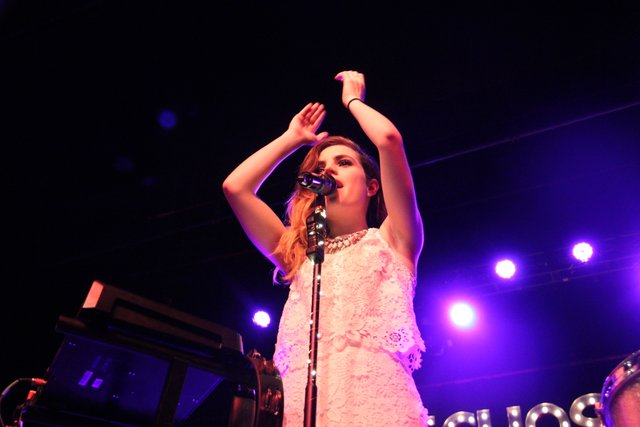 A singer with an arm raised on a stage lit in blue and purple