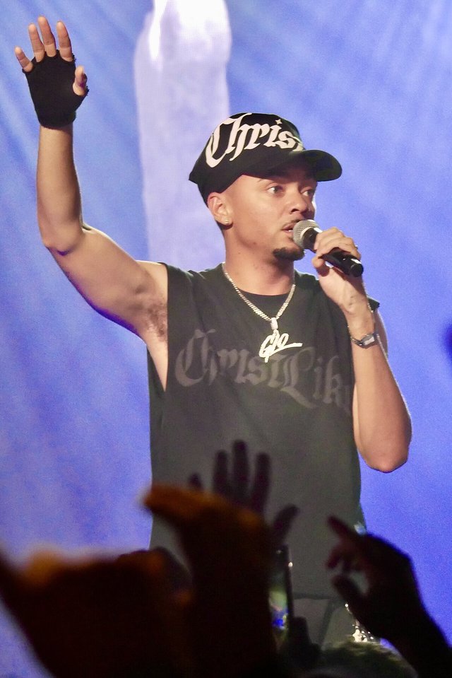 Miles Minnick on stage in a black cap and sleeveless shirt, one gloved hand raised and a microphone in the other