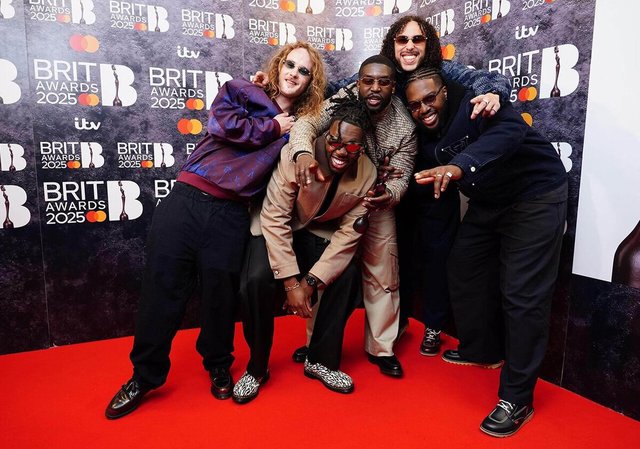 The five members of Ezra Collective posing together on a red carpet in front of a Brit Awards backdrop