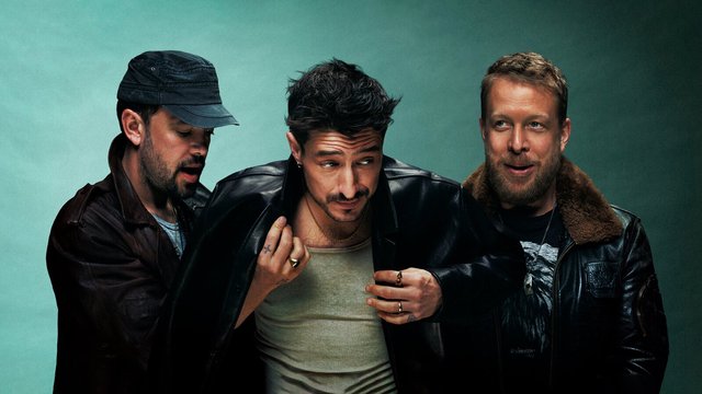 Mumford & Sons, three men in leather jackets, posed shoulder to shoulder against a teal backdrop