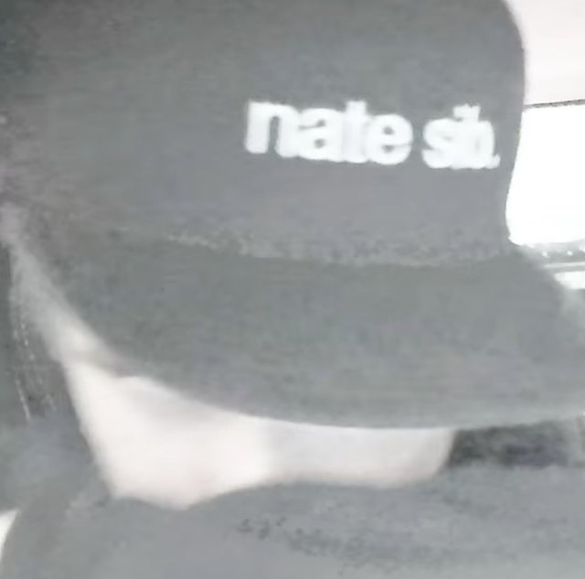 Grainy black-and-white close-up of Nate Sib wearing a dark cap with "nate sib" printed across the front