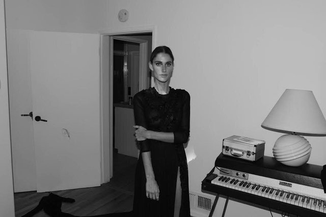 Black and white portrait of Niia standing beside a Rhodes electric piano