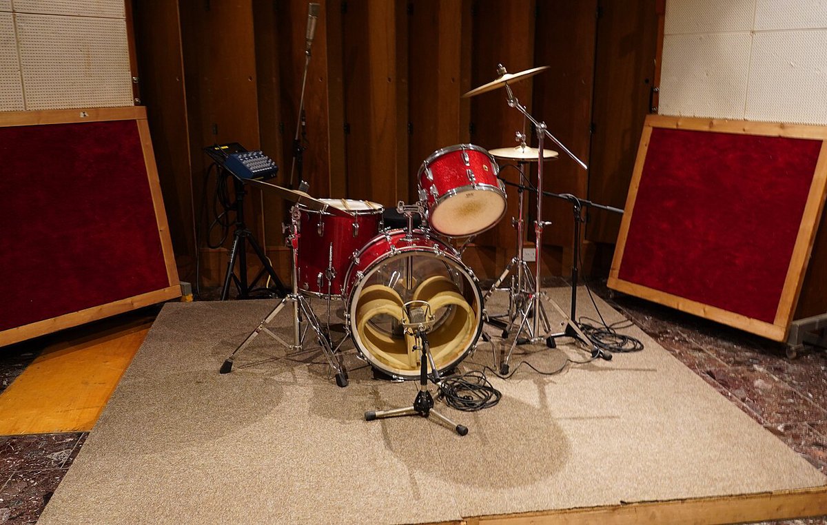 A recording studio live room with a small drum kit set up on a carpet in front of padded wall panels