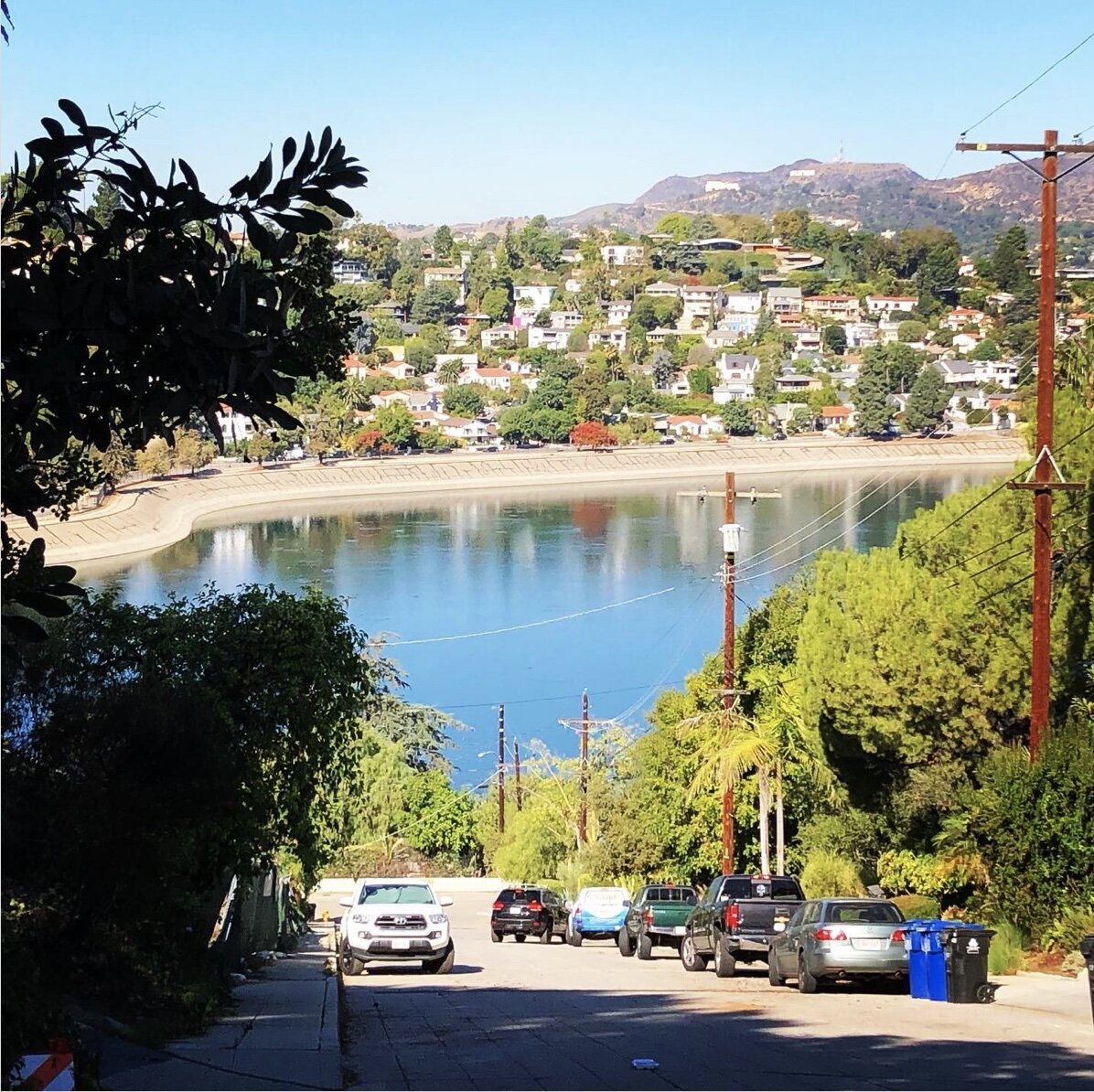 View down a Silver Lake street to the reservoir, with hillside homes and the Hollywood Sign beyond