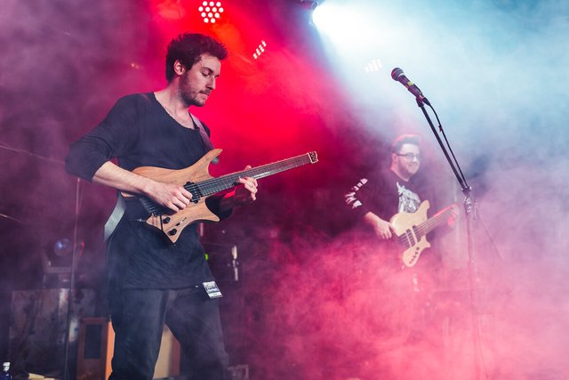 Guitarist on a smoky, red and blue lit stage with a bassist behind him