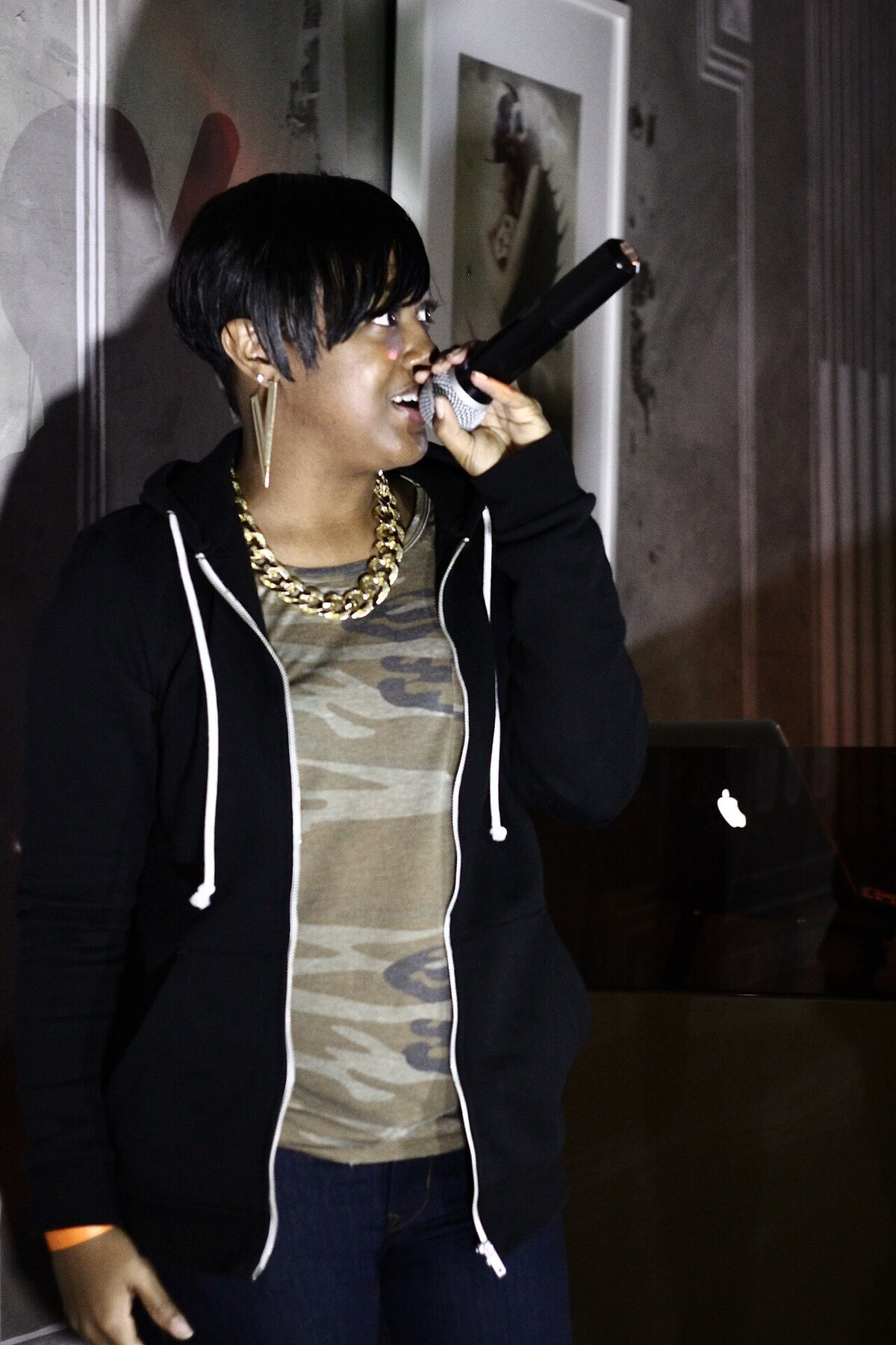 Rapsody performing with a microphone in a black zip-up hoodie and gold chain