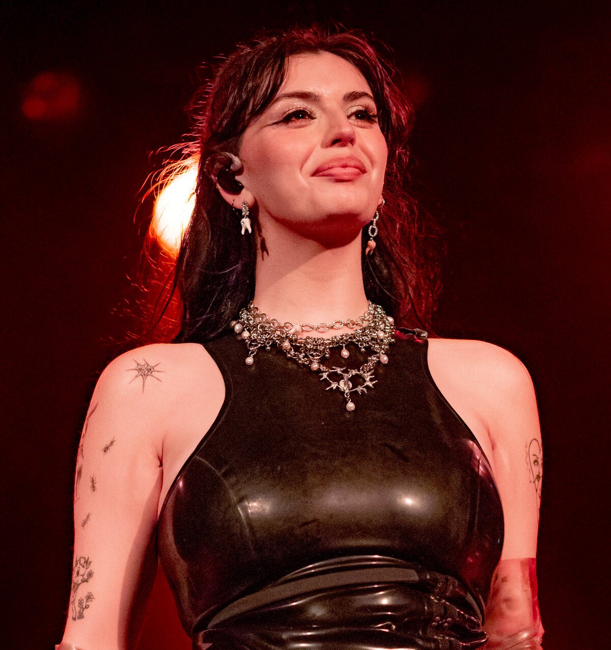 Rebecca Black on stage in black latex top and silver chain necklace under red lighting