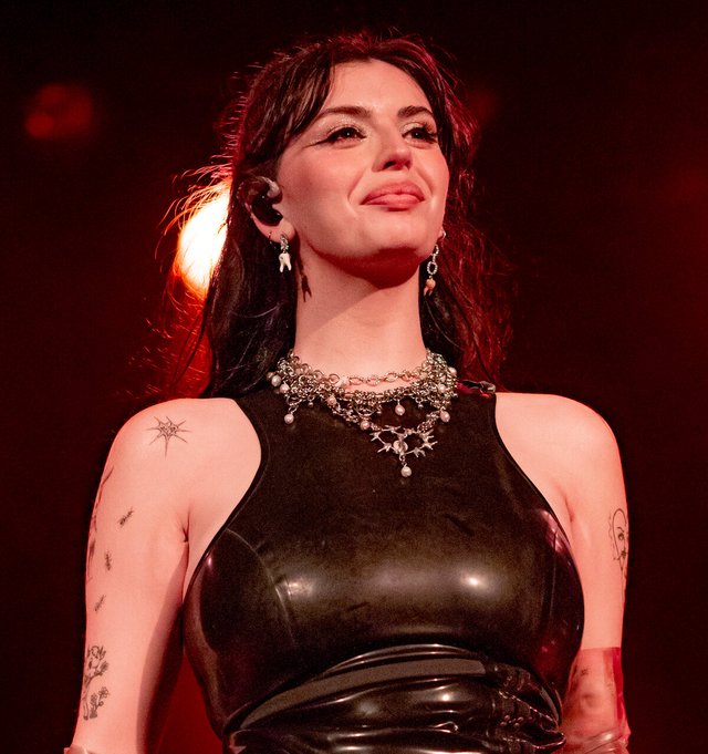 Rebecca Black on stage in black latex top and silver chain necklace under red lighting