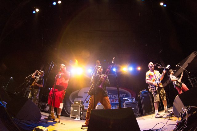 Ska band on a lit stage with a trombone, saxophone and guitars, seen from a low angle