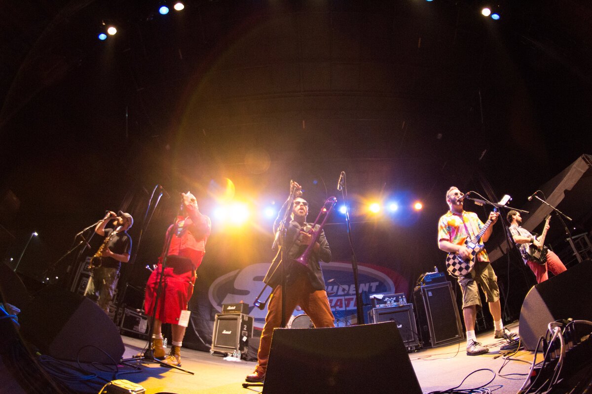 Ska band on a lit stage with a trombone, saxophone and guitars, seen from a low angle