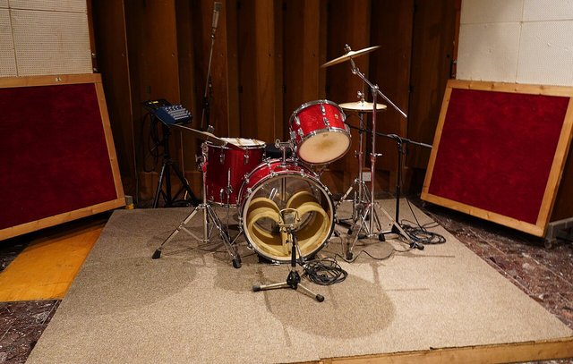 A recording studio live room with a small drum kit set up on a carpet in front of padded wall panels