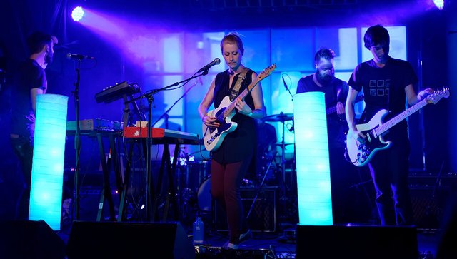 A band performing on a small stage lit in blue with two glowing light panels