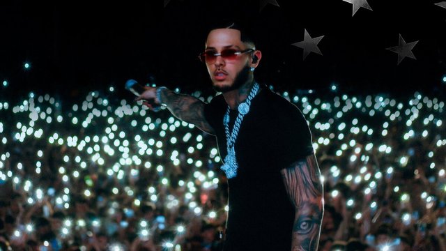 ROA in red-tinted sunglasses and a silver chain pointing a microphone toward a crowd lit by thousands of phone lights