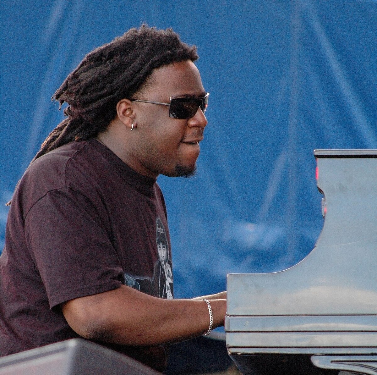 Pianist in sunglasses playing a grand piano in front of a blue backdrop