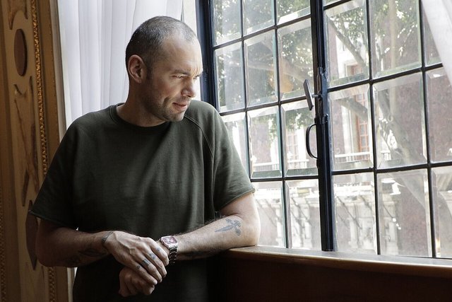 Santiago Cruz glancing out of a tall window in a gilded room