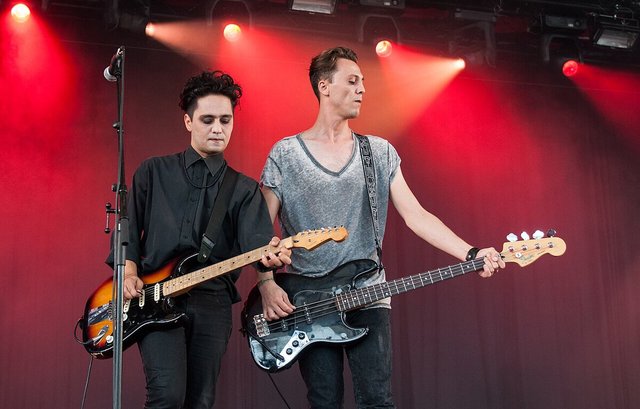 Two members of a dark wave band playing guitar and bass on a stage lit in red