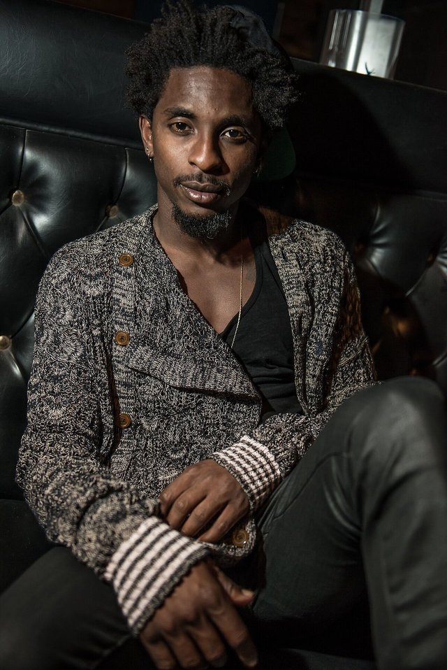 Portrait of the rapper Shwayze seated on a black leather banquette