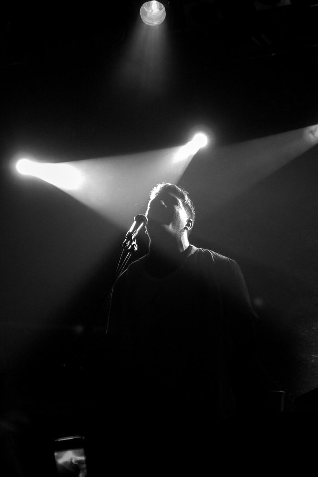 Singer in silhouette at a microphone under bright stage spotlights, black and white