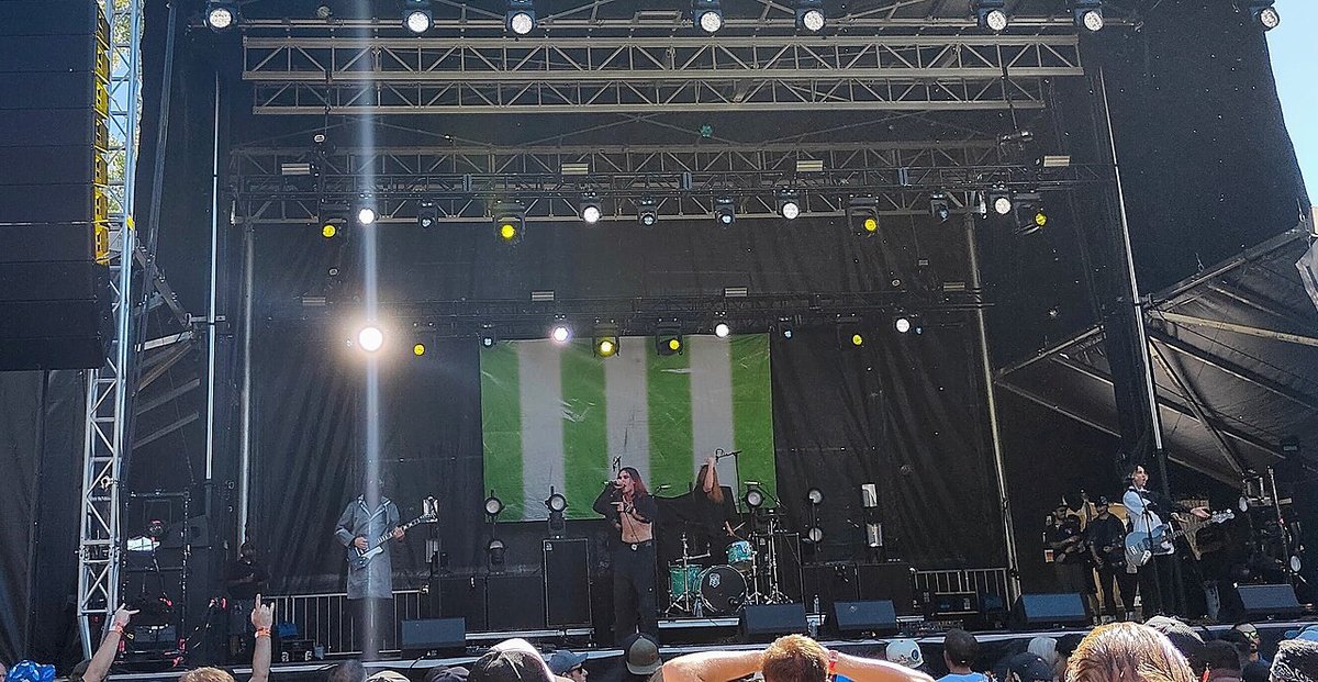 Singer and guitarists performing on an outdoor festival stage under a row of stage lights
