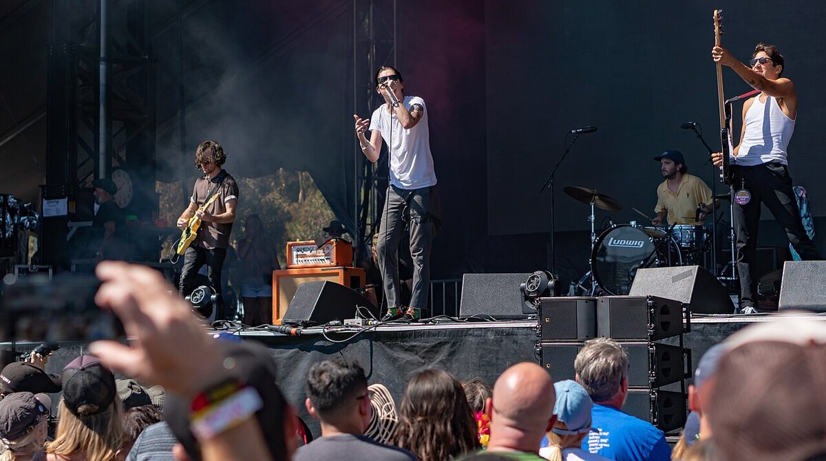 Plague Vendor performing on an outdoor festival stage, a singer at the microphone between a guitarist, a drummer and a bassist, with a crowd in the foreground
