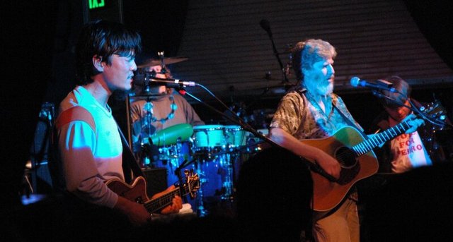 Two guitarists and a drummer on a dimly lit stage during a String Cheese Incident performance