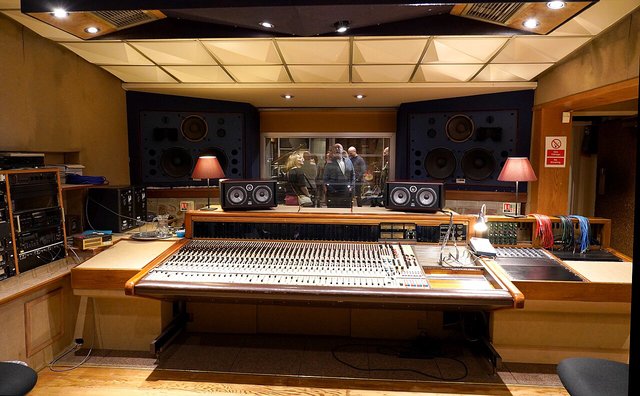 A recording studio control room with a large mixing desk and speaker monitors, with no one in it