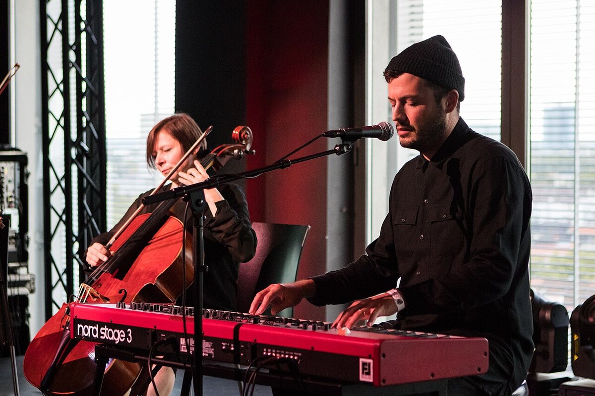 Singer at a red keyboard beside a cellist during a 2017 SYML festival performance